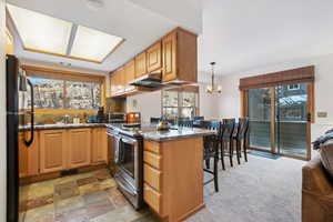 Kitchen with black refrigerator, stainless steel electric range, light carpet, decorative light fixtures, and kitchen peninsula