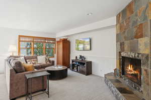 Living room featuring light carpet, a wainscoted wall, and a fireplace