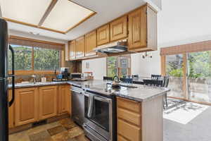 Kitchen with stainless steel appliances, a peninsula, under cabinet range hood, tasteful backsplash, and dark stone finish floors
