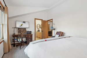 Carpeted bedroom featuring vaulted ceiling and ensuite bathroom