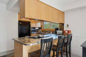 Kitchen with freestanding refrigerator, a peninsula, wainscoting, a kitchen breakfast bar, and light brown cabinetry