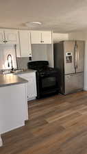 Kitchen with white cabinets, black gas stove, dark wood-type flooring, and stainless steel fridge