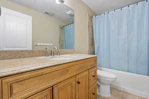 Full bathroom featuring vanity, shower / bathtub combination with curtain, a textured ceiling, and toilet