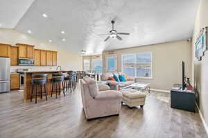 Living room with ceiling fan, lofted ceiling, light hardwood / wood-style flooring, and a textured ceiling