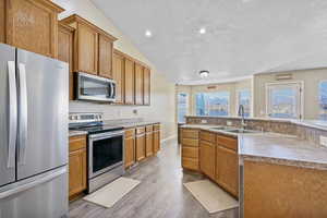 Kitchen with sink, a textured ceiling, an island with sink, hardwood / wood-style flooring, and stainless steel appliances