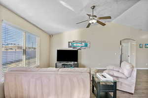 Living room with vaulted ceiling, ceiling fan, hardwood / wood-style floors, and a textured ceiling