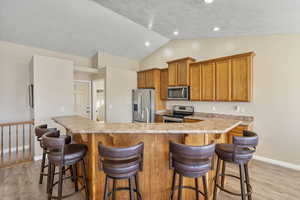 Kitchen featuring stainless steel appliances, vaulted ceiling, a breakfast bar area, and light hardwood / wood-style floors