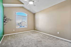 Carpeted empty room featuring ceiling fan and vaulted ceiling