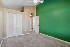 Unfurnished bedroom with ceiling fan, high vaulted ceiling, a textured ceiling, light carpet, and a closet