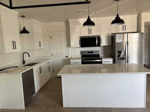 Kitchen featuring appliances with stainless steel finishes, a center island, pendant lighting, and white cabinets