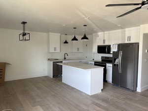 Kitchen with white cabinets, decorative light fixtures, a kitchen island, and black appliances