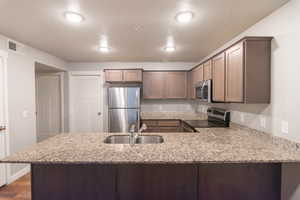 Kitchen featuring sink, stainless steel appliances, light stone counters, and kitchen peninsula