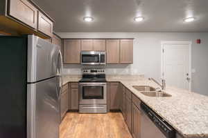 Kitchen with light stone countertops, light hardwood / wood-style floors, sink, kitchen peninsula, and stainless steel appliances