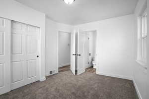 Unfurnished bedroom with a closet, connected bathroom, and dark colored carpet