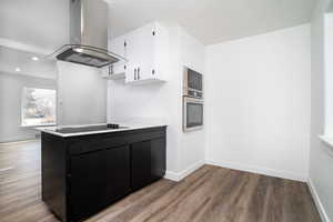 Kitchen featuring white cabinetry, island range hood, hardwood / wood-style flooring, stainless steel oven, and built in microwave