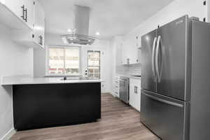 Kitchen with decorative backsplash, island exhaust hood, white cabinetry, light hardwood / wood-style flooring, and appliances with stainless steel finishes