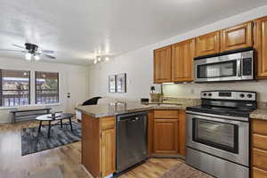 Kitchen with sink, light hardwood / wood-style floors, kitchen peninsula, stainless steel appliances, and a textured ceiling