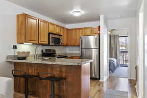 Kitchen with sink, light wood-type flooring, kitchen peninsula, stainless steel appliances, and a textured ceiling