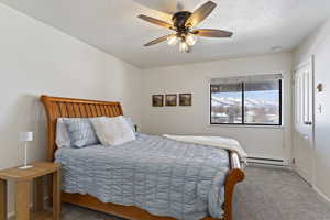 Carpeted bedroom with a textured ceiling, a baseboard radiator, and ceiling fan