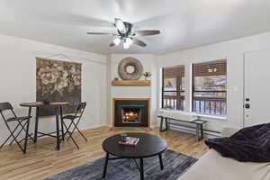 Living room with ceiling fan, a textured ceiling, baseboard heating, and light wood-type flooring