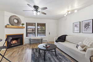 Living room featuring ceiling fan, a baseboard heating unit, a textured ceiling, and light wood-type flooring