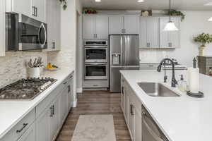 Kitchen featuring appliances with stainless steel finishes, pendant lighting, tasteful backsplash, sink, and dark hardwood / wood-style flooring