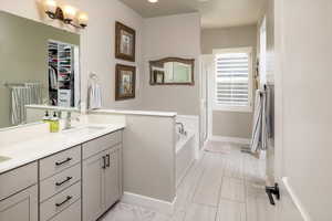 Bathroom featuring a relaxing tiled tub, vanity, and tile patterned flooring