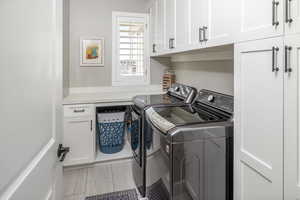 Clothes washing area featuring cabinets, washing machine and dryer, and tile patterned flooring