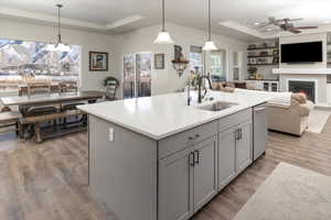 Kitchen featuring gray cabinets, pendant lighting, an island with sink, sink, and a raised ceiling