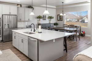 Kitchen featuring pendant lighting, sink, appliances with stainless steel finishes, white cabinetry, and an island with sink