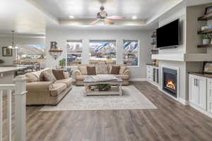 Living room featuring dark hardwood / wood-style flooring, a tray ceiling, and ceiling fan with notable chandelier