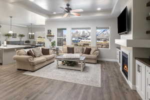 Living room with ceiling fan with notable chandelier, dark wood-type flooring, and a raised ceiling