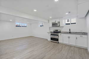 Kitchen featuring stainless steel appliances, light stone countertops, light hardwood / wood-style flooring, and white cabinets