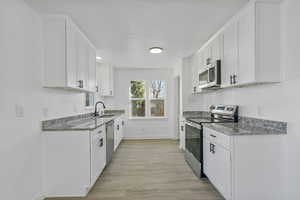 Kitchen featuring sink, light stone counters, light wood-type flooring, appliances with stainless steel finishes, and white cabinets