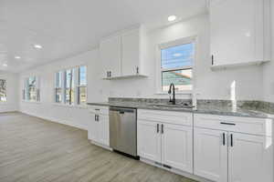 Kitchen with sink, white cabinetry, light wood-type flooring, dishwasher, and light stone countertops