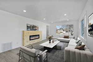 Living room featuring a glass covered fireplace, visible vents, recessed lighting, and wood finished floors