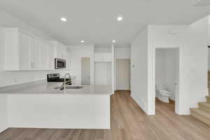 Kitchen with appliances with stainless steel finishes, kitchen peninsula, light hardwood / wood-style floors, and white cabinets