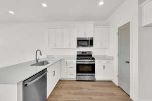 Kitchen featuring sink, stainless steel appliances, light hardwood / wood-style floors, and white cabinets