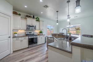 Kitchen with sink, stainless steel appliances, tasteful backsplash, white cabinets, and decorative light fixtures