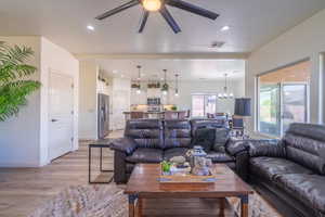 Living room with ceiling fan with notable chandelier, a textured ceiling, and light wood-type flooring