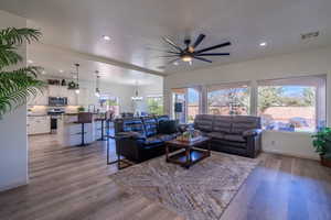 Living room featuring ceiling fan with notable chandelier, sink, light hardwood / wood-style flooring, and a textured ceiling