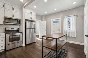 Kitchen with white cabinetry, appliances with stainless steel finishes, dark hardwood / wood-style floors, and backsplash