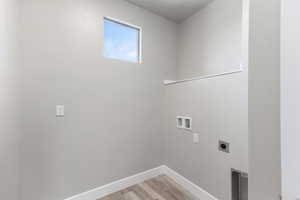 Clothes washing area with hookup for a washing machine, light hardwood / wood-style flooring, and hookup for an electric dryer