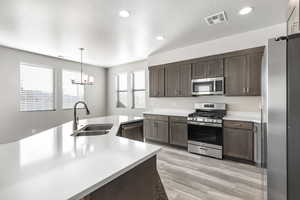 Kitchen featuring stainless steel appliances, sink, pendant lighting, and dark brown cabinetry