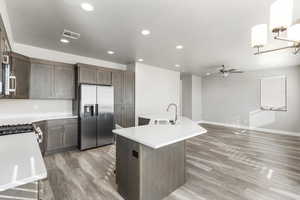 Kitchen with sink, stainless steel fridge, a kitchen island with sink, ceiling fan, and light hardwood / wood-style floors