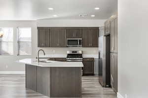 Kitchen featuring sink, light hardwood / wood-style flooring, appliances with stainless steel finishes, a kitchen island with sink, and dark brown cabinets