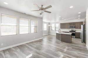 Kitchen featuring ceiling fan, a kitchen island with sink, stainless steel appliances, dark brown cabinetry, and decorative light fixtures