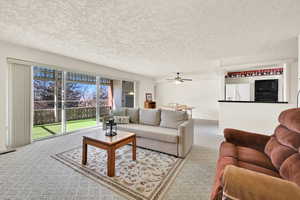 Carpeted living room with ceiling fan and a textured ceiling