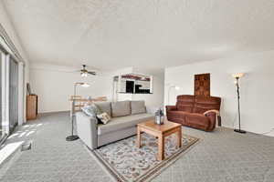 Living room with ceiling fan, a textured ceiling, and light carpet