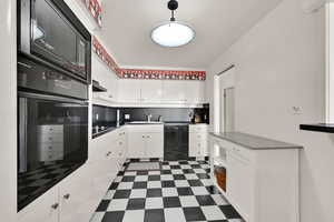 Kitchen with hanging light fixtures, sink, white cabinets, tasteful backsplash, and black appliances